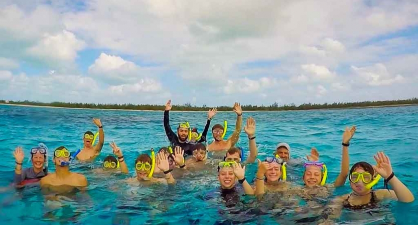 a group of gap year students wearing snorkles stand in blue water and raise their hands in celebration 